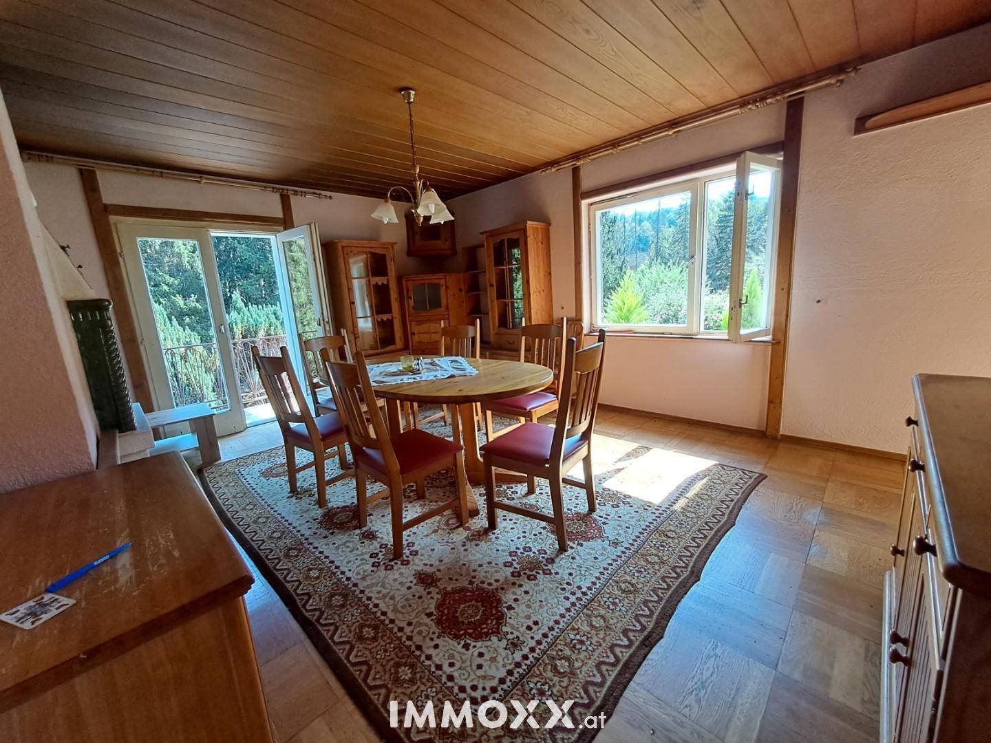 Traditioneller Essbereich mit Holztisch, Stühlen, Kachelofen und Zugang zum Balkon.