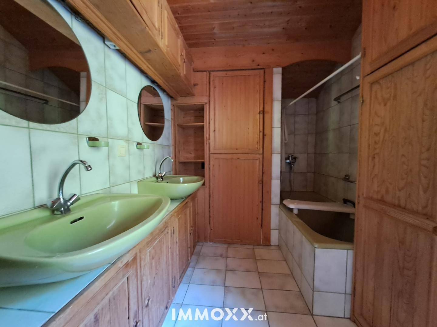 Badezimmer im 80er-Jahre-Stil mit Doppelwaschbecken, Badewanne und Holzverkleidung.