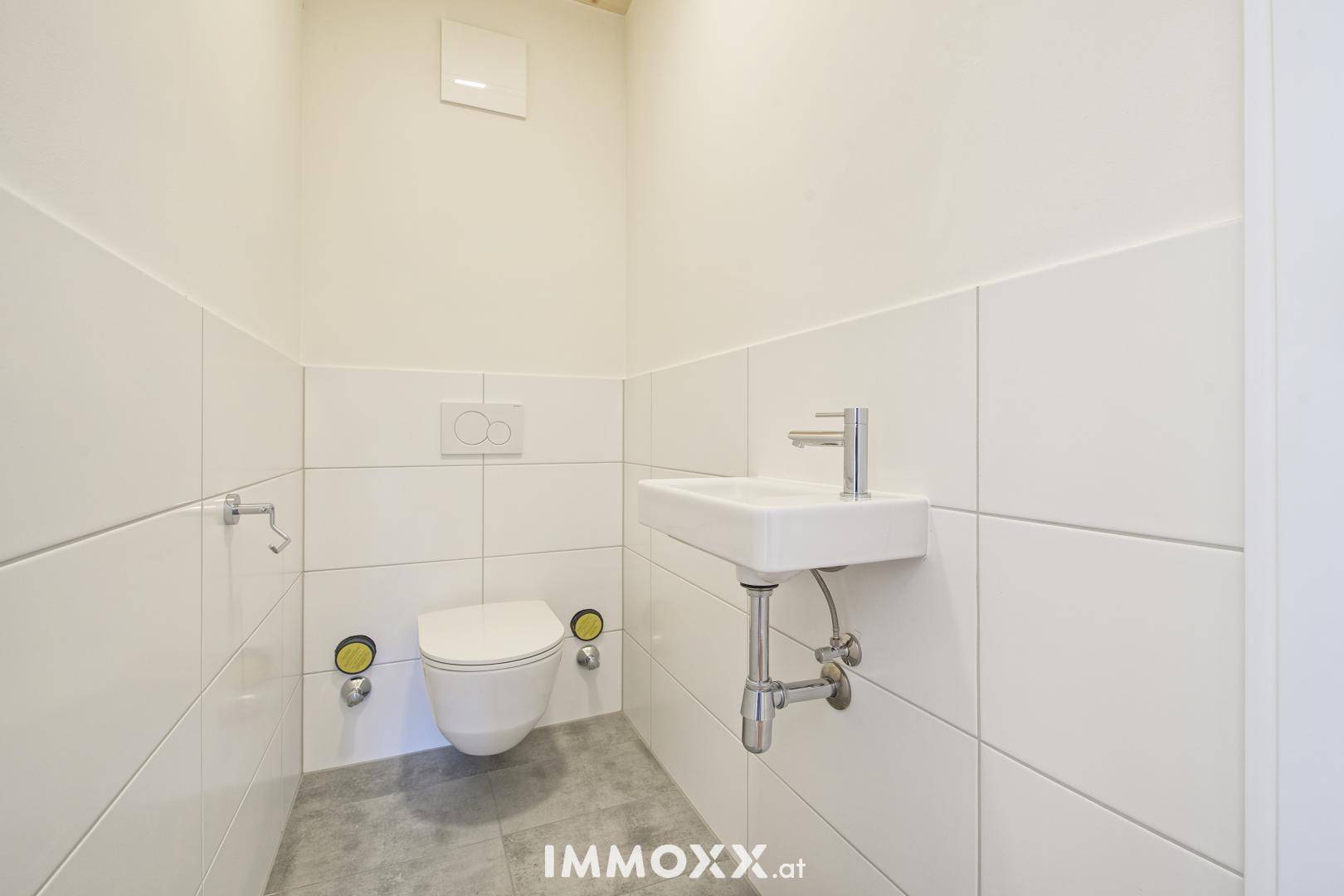 Modernes Gäste-WC mit wandhängendem WC, kleinem Waschbecken und weißen Fliesen.