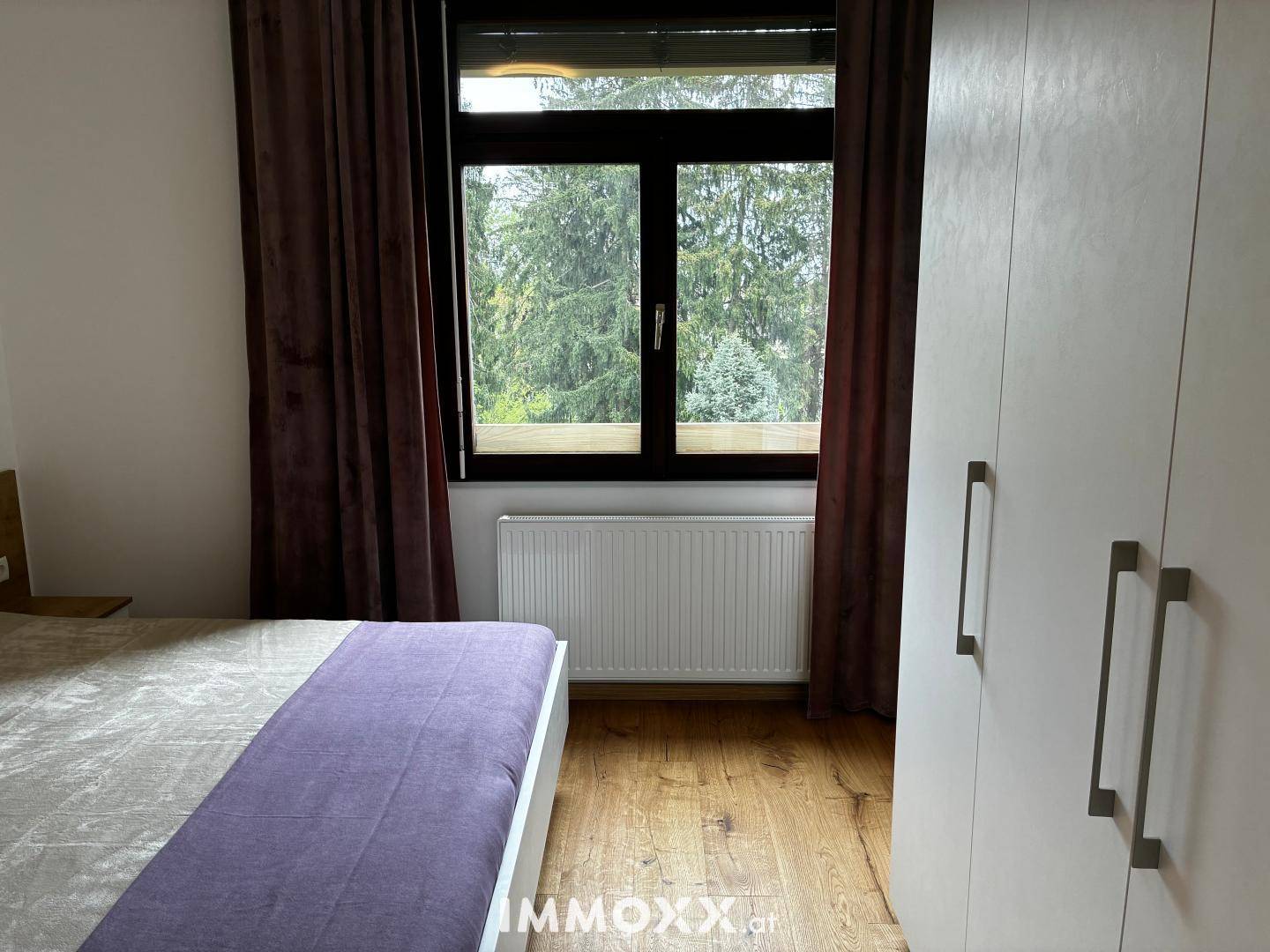 Schlafzimmer mit großem weißen Kleiderschrank und Fenster, das viel Tageslicht hereinlässt.