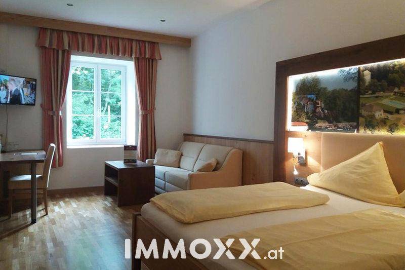 Gemütliches Schlafzimmer mit Holzboden, Doppelbett und einem kleinen Sofa am Fenster mit Blick ins Grüne.