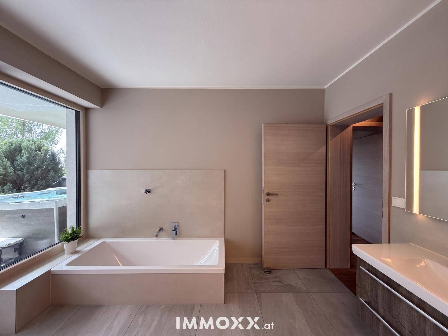 Modernes Badezimmer mit großer Badewanne, stilvollem Waschtisch und Fenster mit Blick ins Freie.