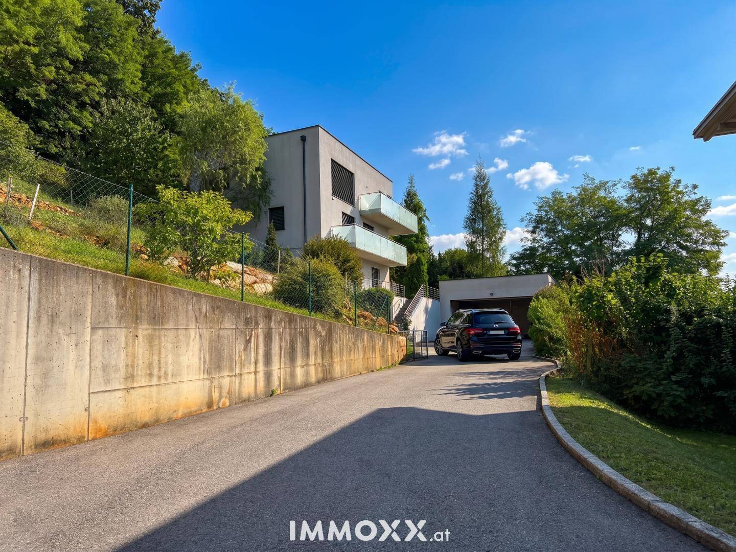 Zufahrt zur modernen Villa mit Garage, umgeben von üppiger grüner Vegetation.