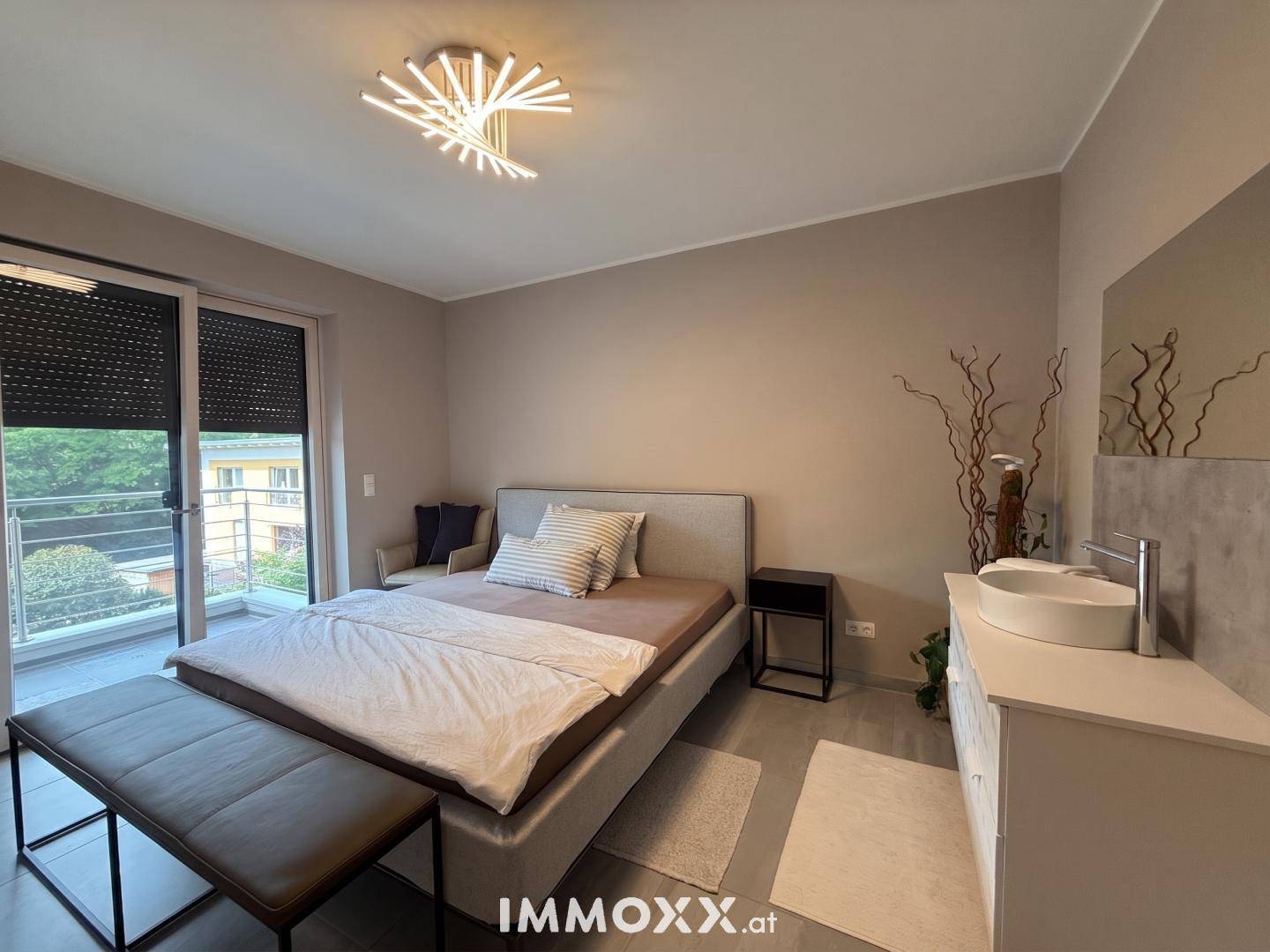 Helles Schlafzimmer mit Balkonzugang, modernem Bett und integriertem Waschbeckenbereich.