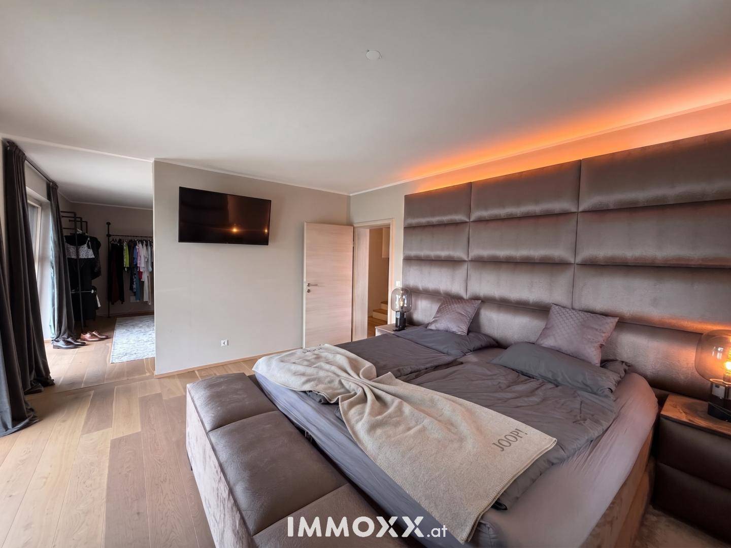 Luxuriöses Schlafzimmer mit großem Polsterbett, indirekter Beleuchtung und Holzboden.