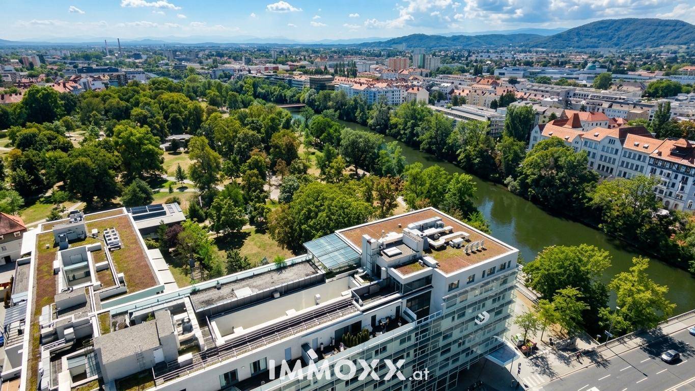Luftaufnahme eines modernen Gebäudes mit Glasfassade, begrünten Dächern und Flussnähe.
