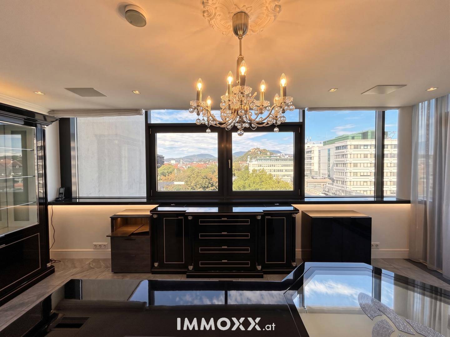 Elegantes Arbeitszimmer mit großen Fenstern, dunklen Möbeln und einem glitzernden Kronleuchter.