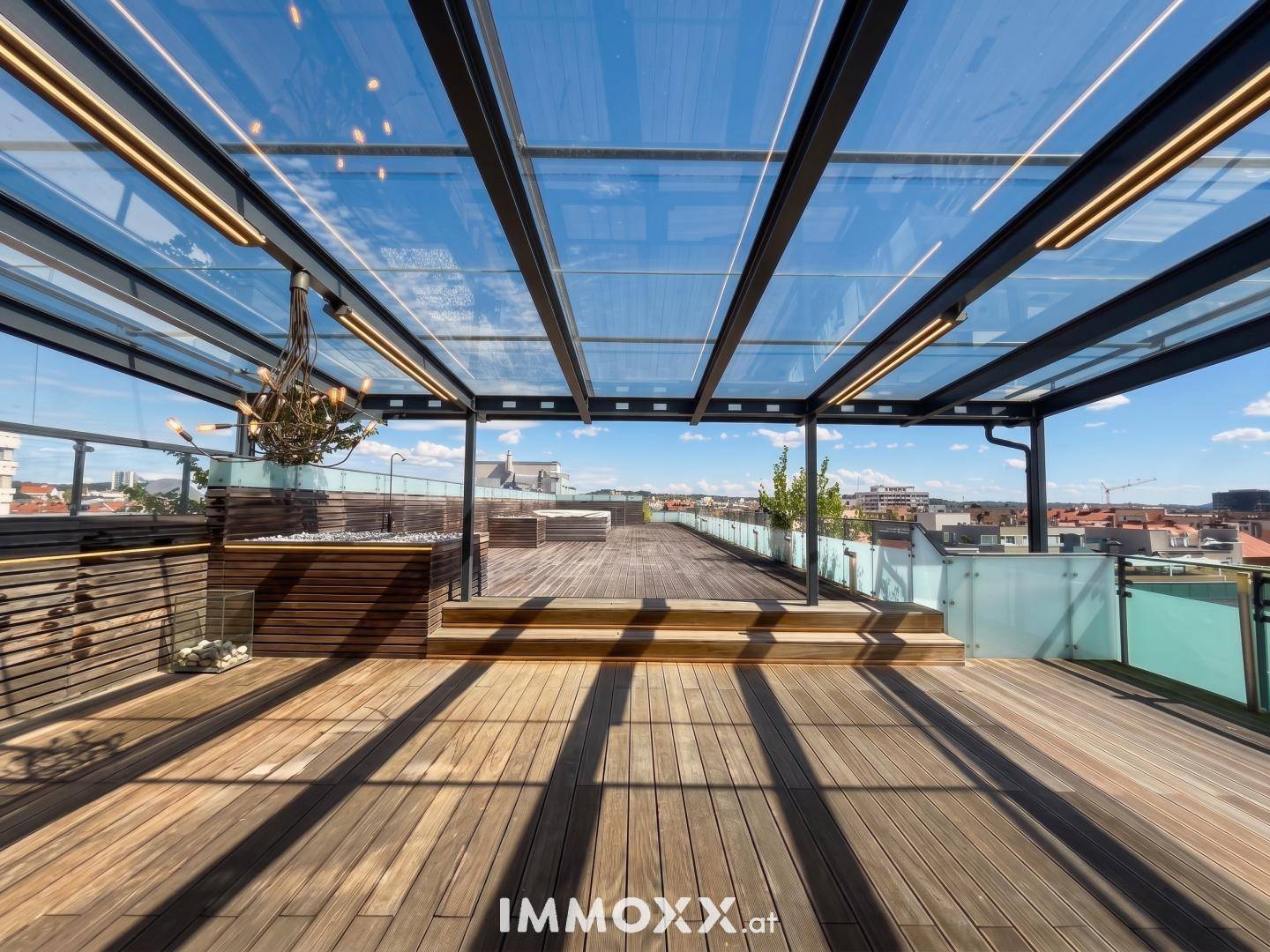 Geräumige Dachterrasse mit Holzdeck, Glasüberdachung und weitem Stadtblick.
