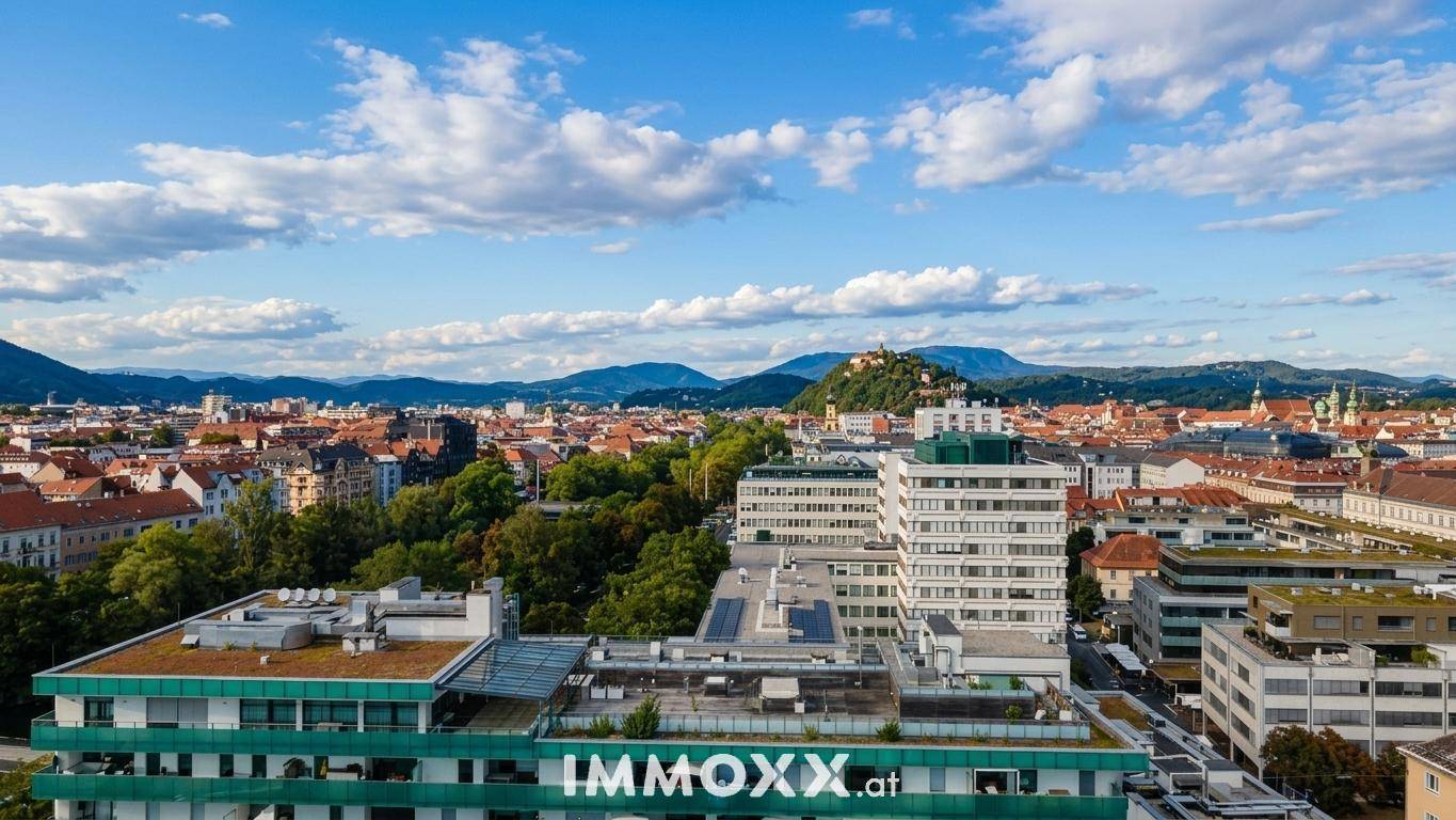 Weitläufiger Blick über die Stadt mit Gebäuden, grünen Flächen und Bergen am Horizont.