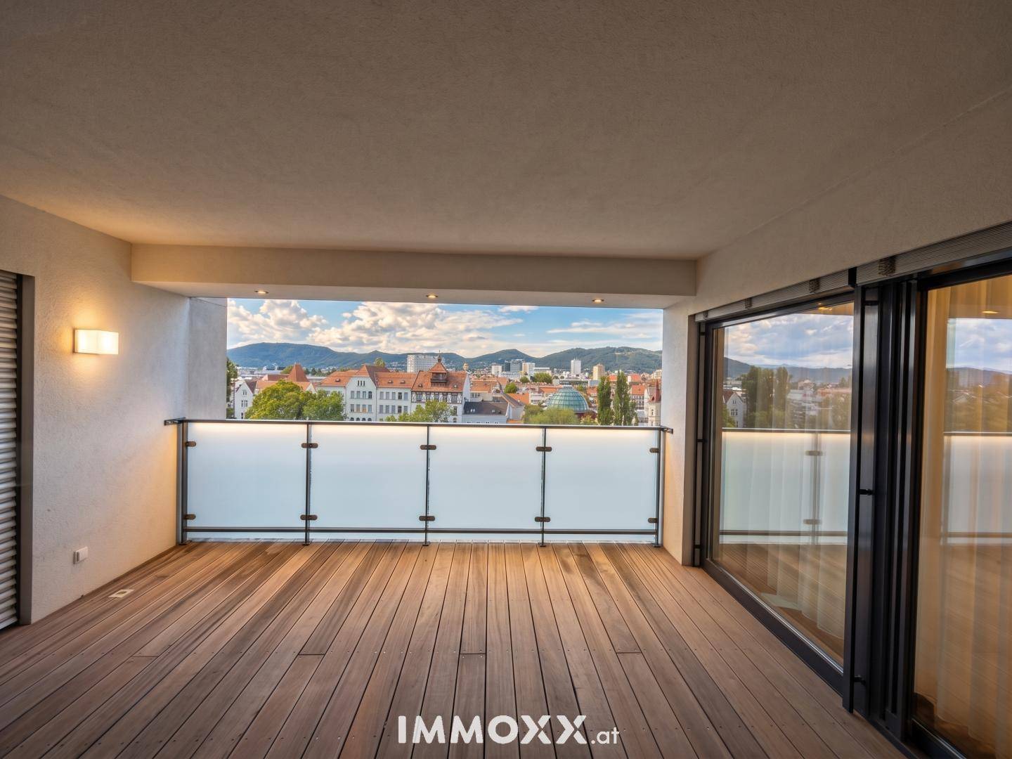 Geräumiger Balkon mit Holzdeck, Glasgeländer und Panoramablick über die Stadt.