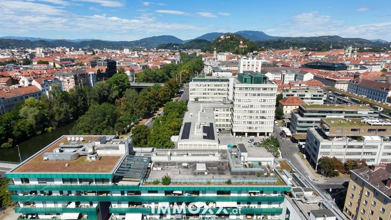 Weitläufige Luftaufnahme der Stadt mit Fluss, Gebäuden und grüner Berglandschaft.