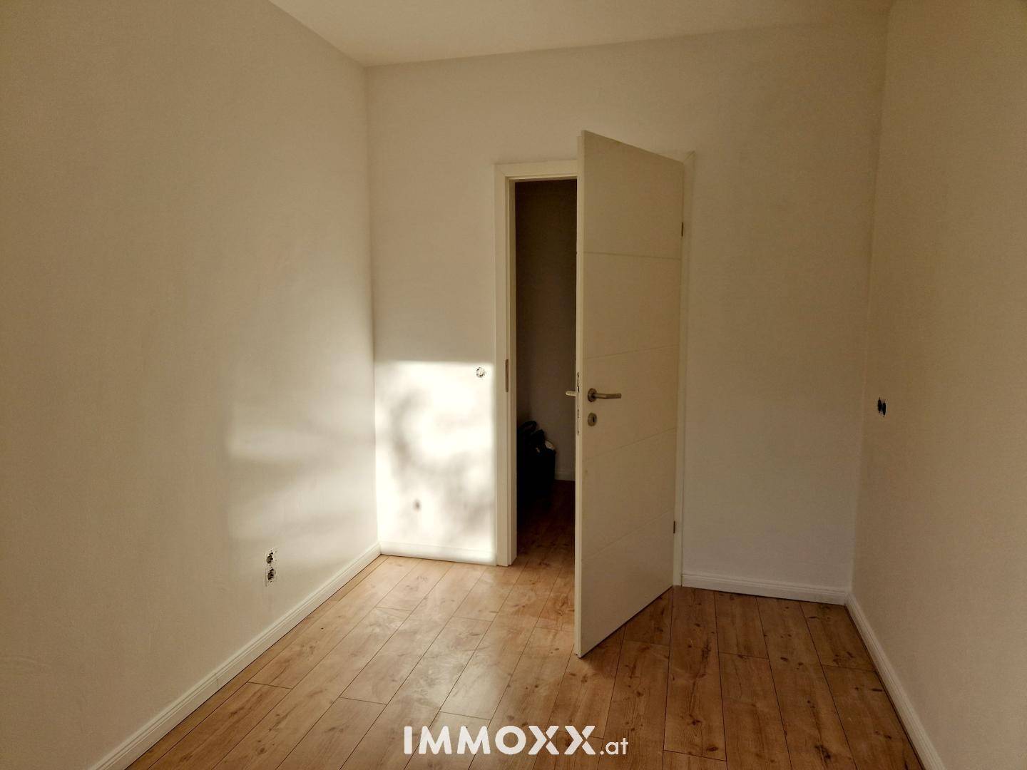 Leeres Zimmer mit Holzboden und weiß gestrichenen Wänden, bereit zur individuellen Gestaltung.