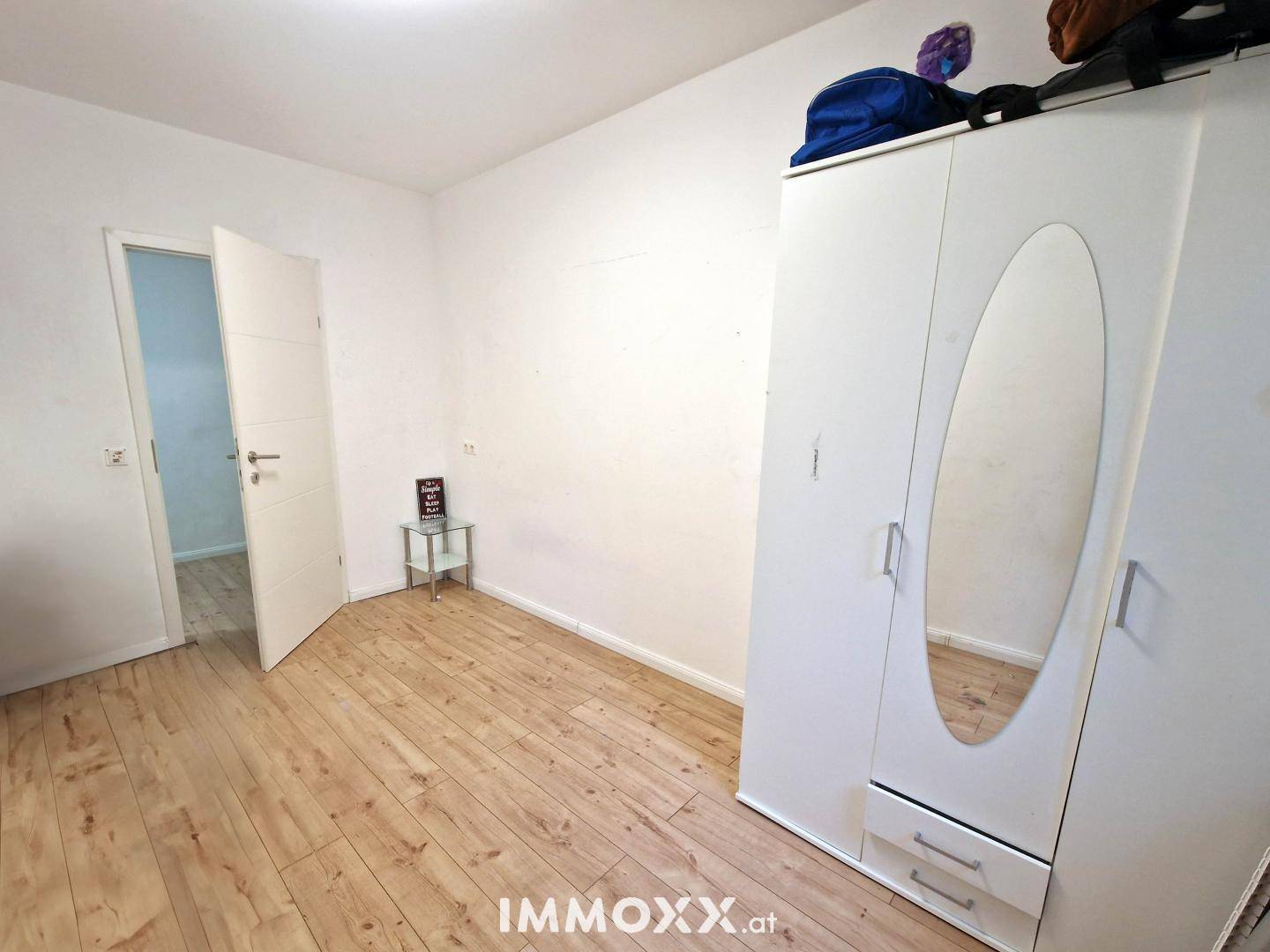 Leeres Schlafzimmer mit hellem Holzboden und einem weißen Kleiderschrank mit Spiegeltür.