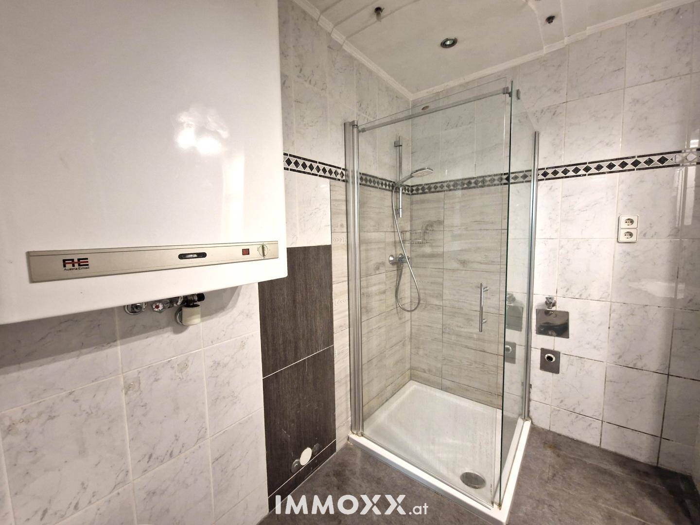 Badezimmer mit Duschkabine, Wandheizung und Fliesen in Weiß und Dunkelgrau.
