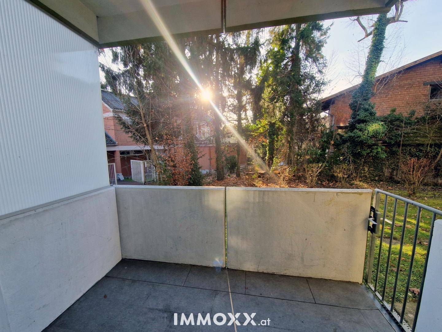 Sonniger Balkon mit Betonbrüstung und Blick ins Grüne, ideal zum Entspannen im Freien.