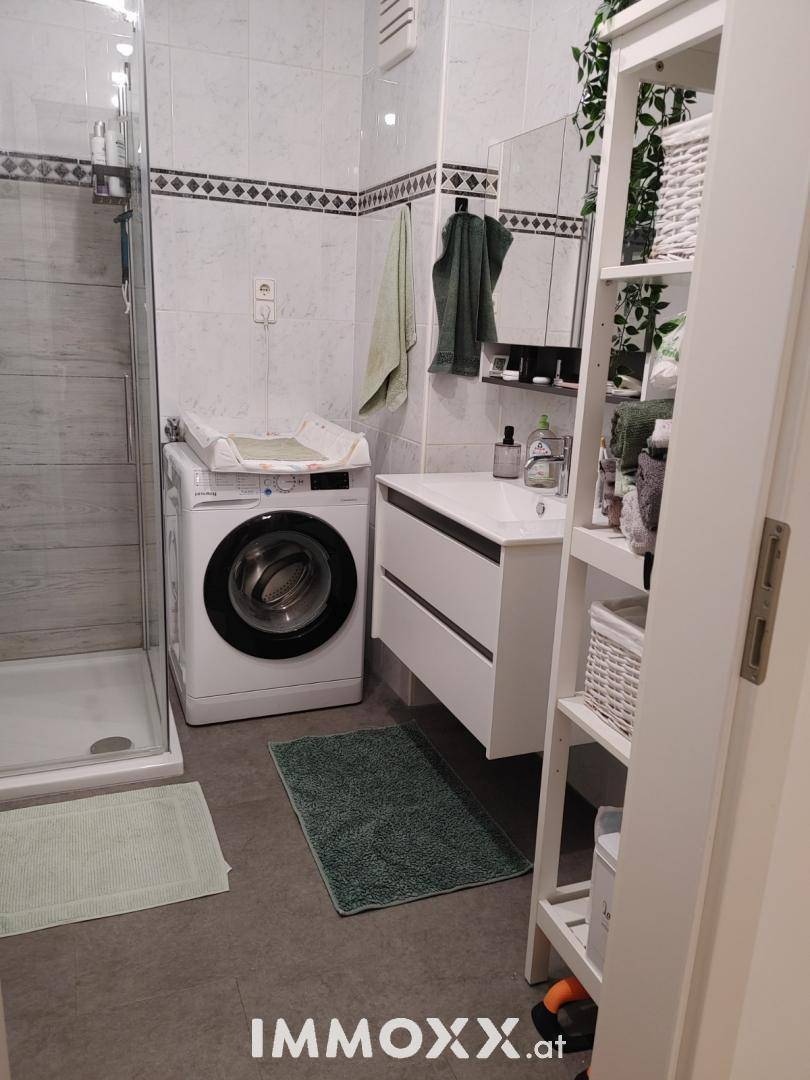 Modernes Badezimmer mit Duschkabine, Waschbeckenunterschrank und Waschmaschine.