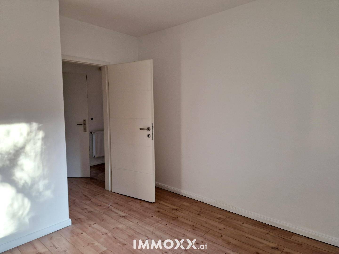 Leeres Zimmer mit Holzboden und weiß gestrichenen Wänden, ideal als Kinder- oder Arbeitszimmer.