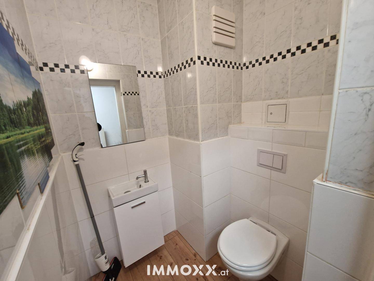 Kleines Gäste-WC mit Toilette, Handwaschbecken und weiß-schwarz gefliesten Wänden.