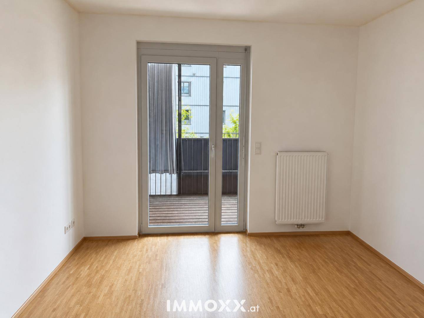 Leerer Raum mit Holzboden, Heizkörper und Zugang zu einem Balkon.