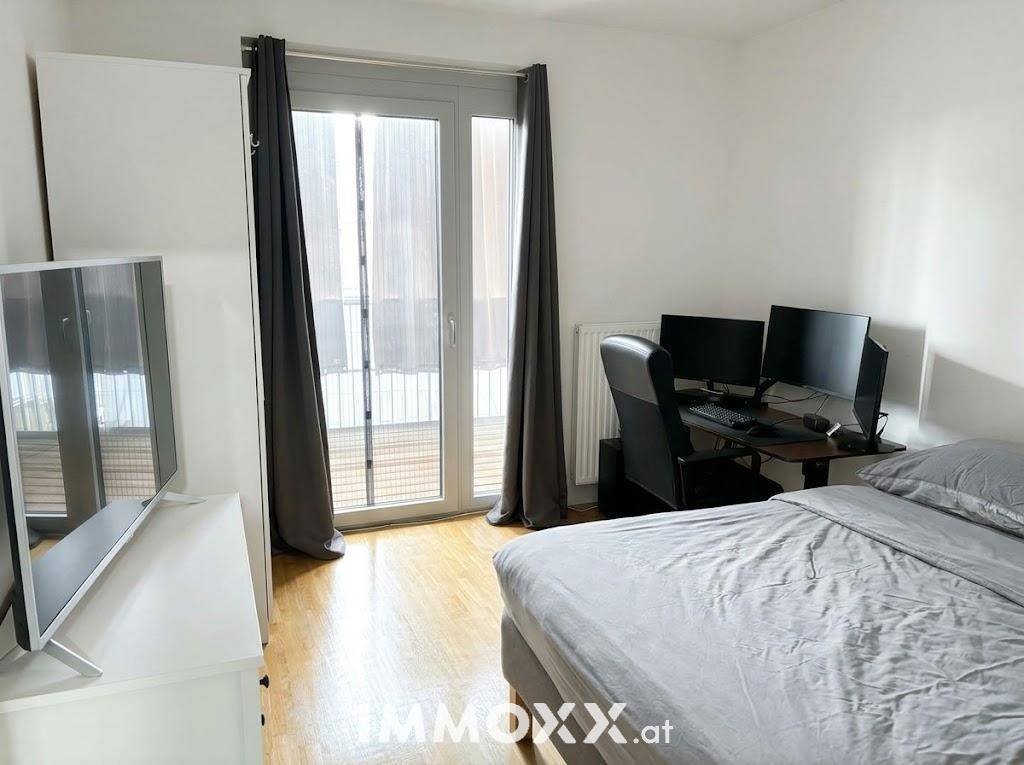 Schlafzimmer mit Bett, Schreibtisch, Fernseher und Zugang zu einem Balkon.
