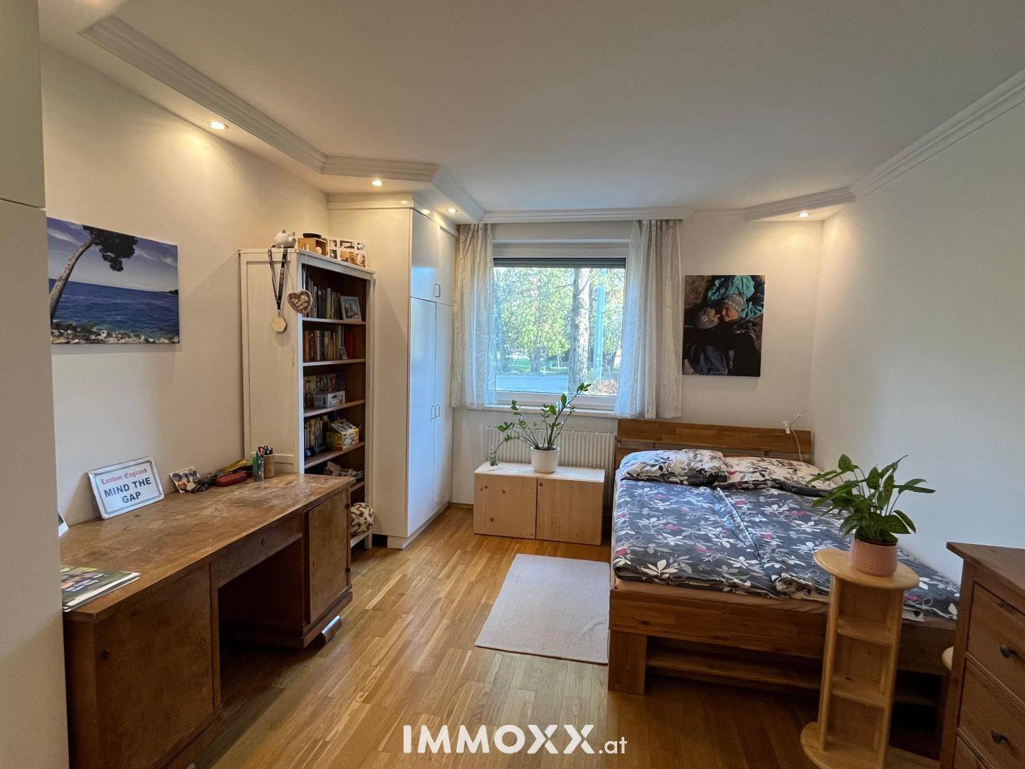 Helles Schlafzimmer mit Holzboden, Schreibtisch und Blick ins Grüne.