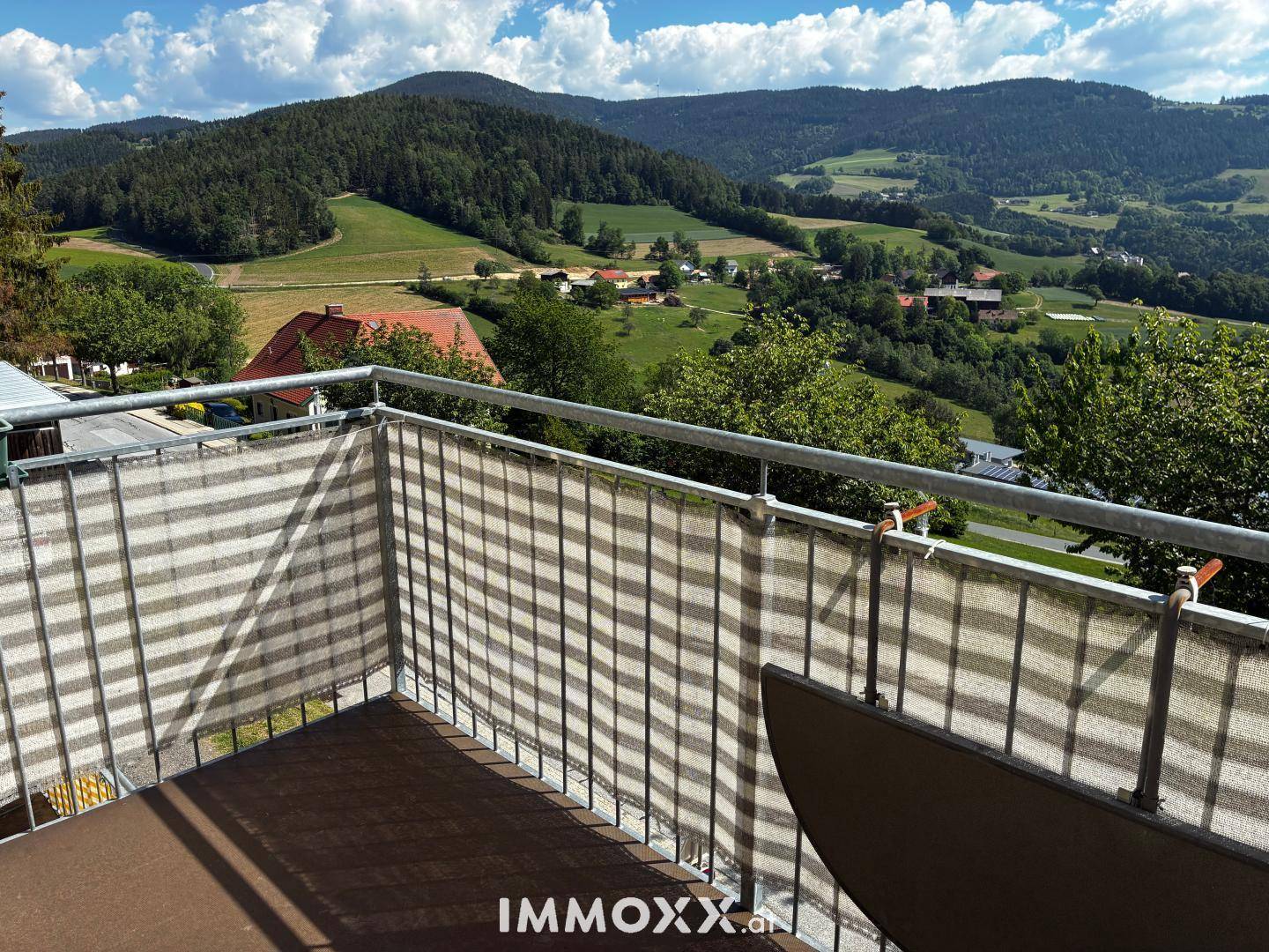 Sonniger Balkon mit weitem Panoramablick über die grüne Landschaft und die umliegenden Berge.
