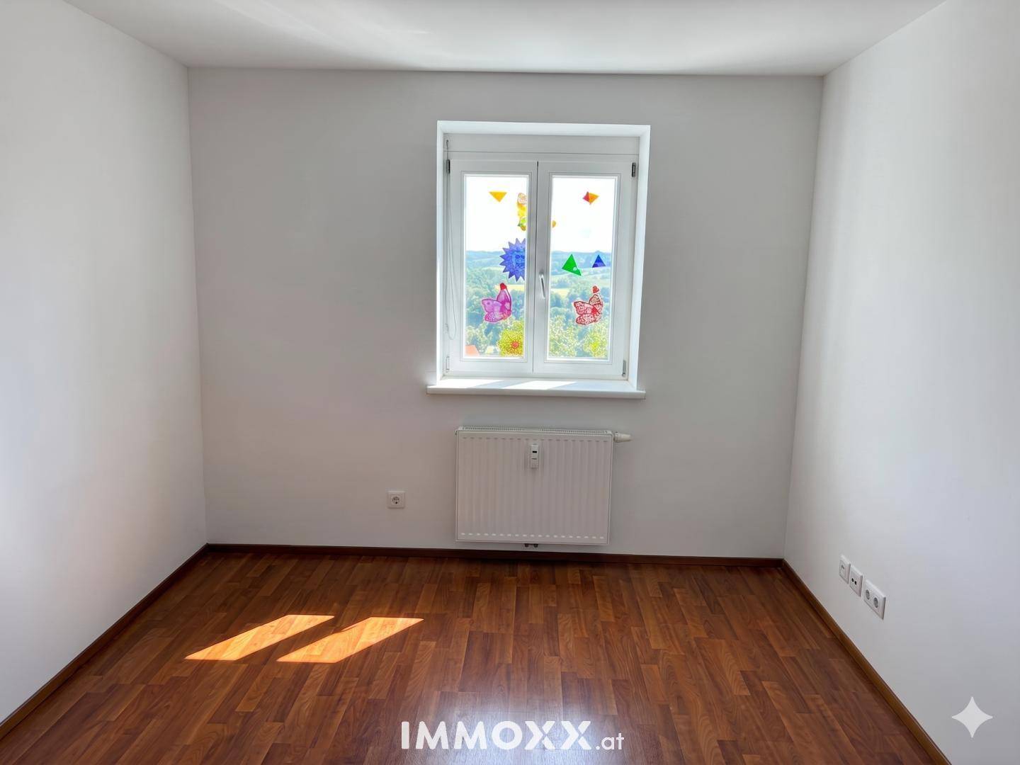 Helles Zimmer mit Laminatboden und einem Fenster, das einen weiten Blick ins Grüne bietet.
