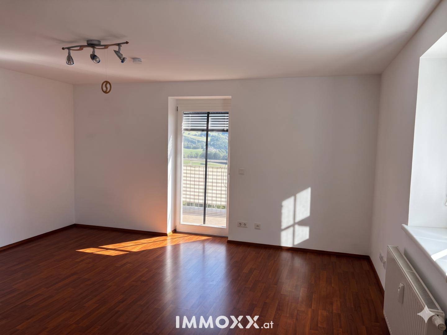 Geräumiges Wohnzimmer mit Laminatboden und direktem Zugang zu einem sonnigen Balkon.