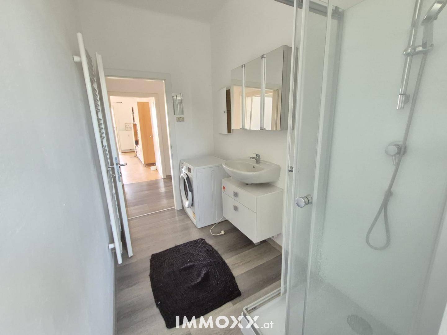 Modernes Badezimmer mit Duschkabine, Waschbecken und Waschmaschine, praktisch und hell gestaltet.