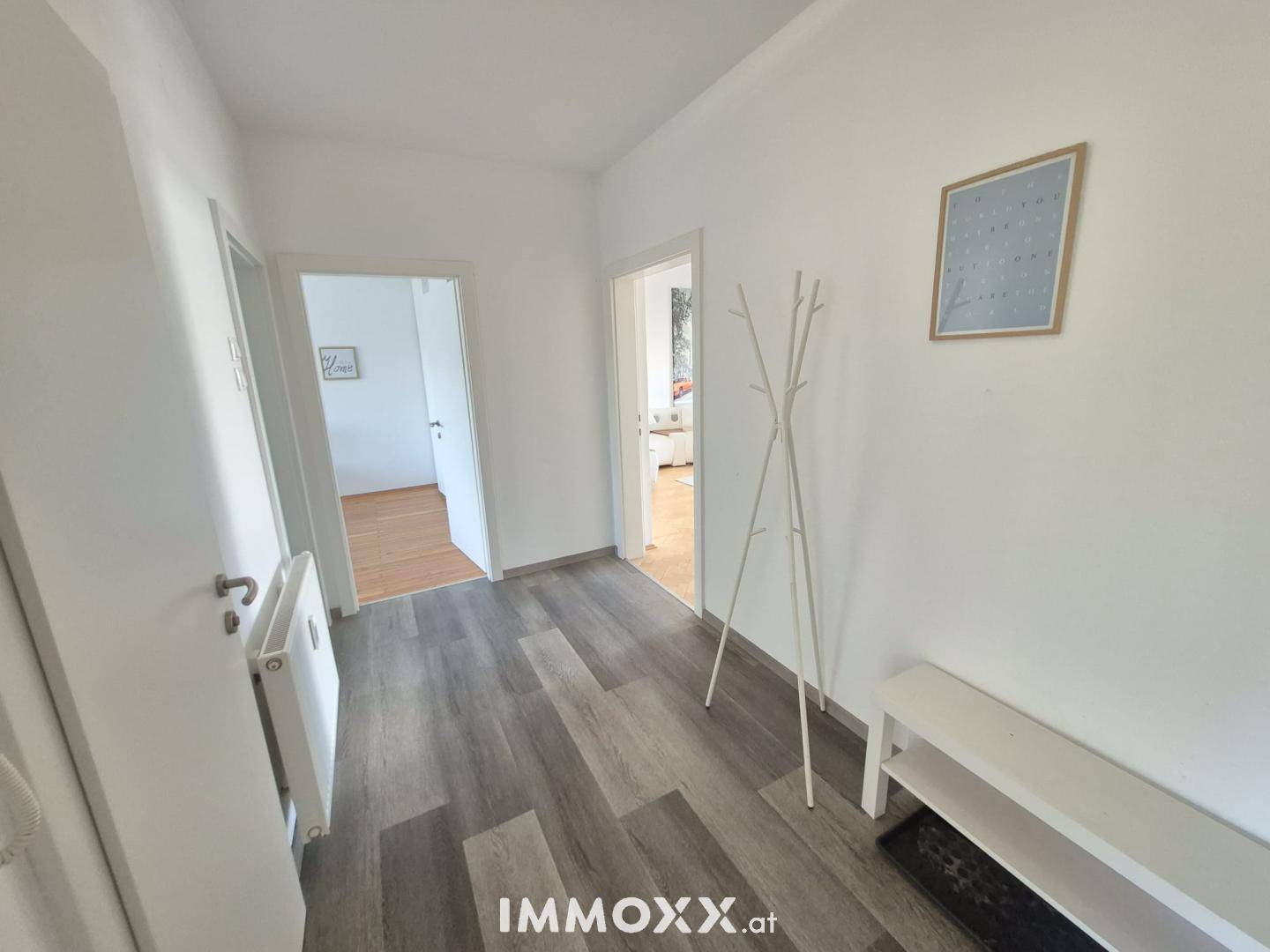 Heller Flur mit modernem Laminatboden und weiß gestrichenen Wänden, führt zu weiteren Räumen.