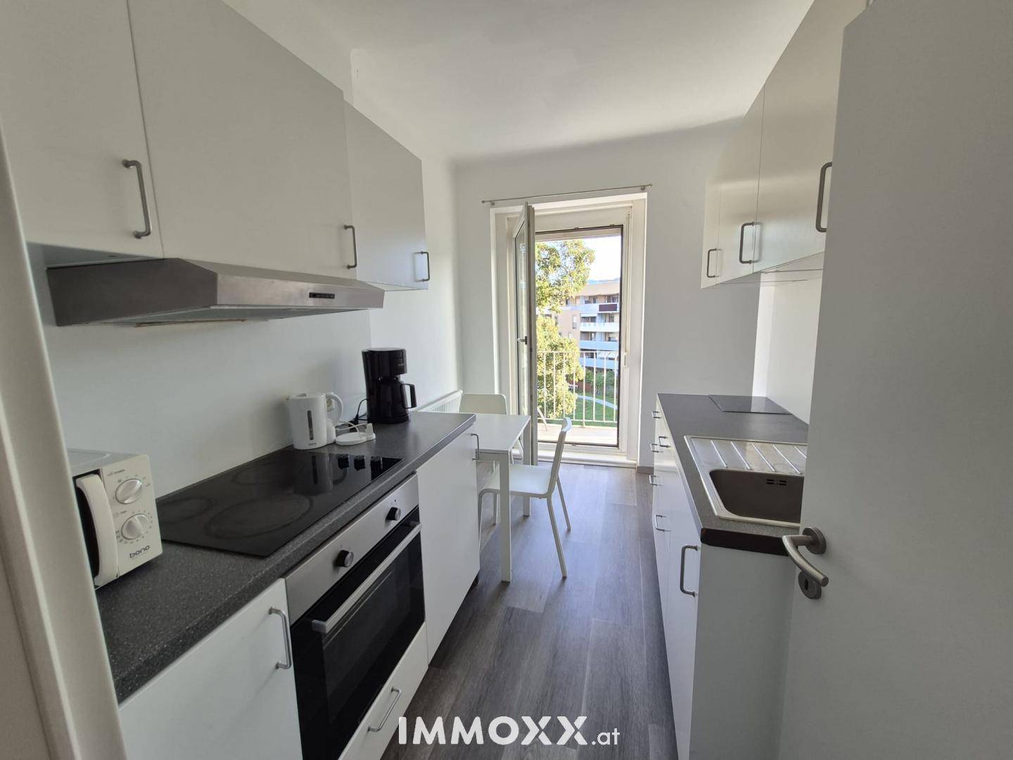 Moderne Küche mit weißen Schränken, dunkler Arbeitsplatte und Essbereich, mit Zugang zum Balkon.