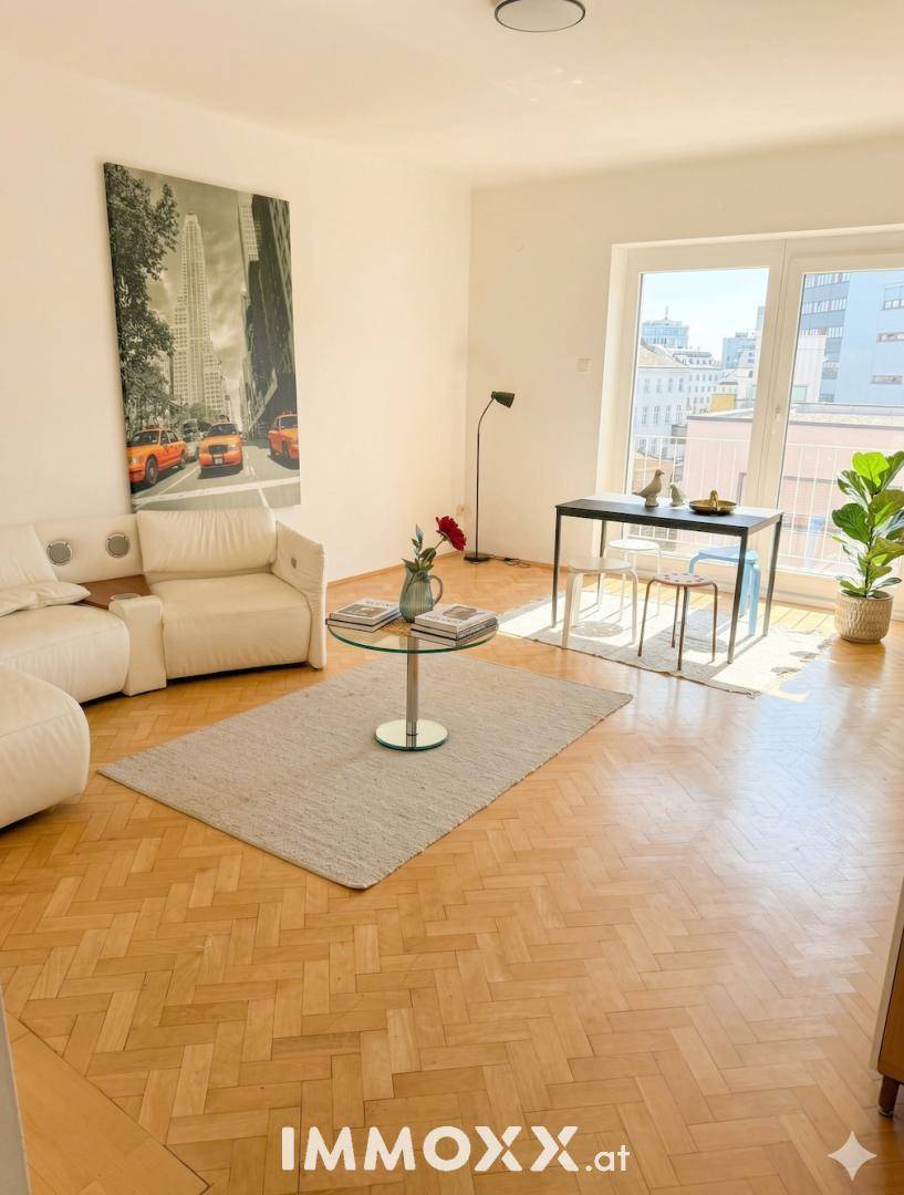 Helles Wohnzimmer mit Fischgrätparkett, weißem Sofa und Essbereich, bietet einen schönen Stadtblick.