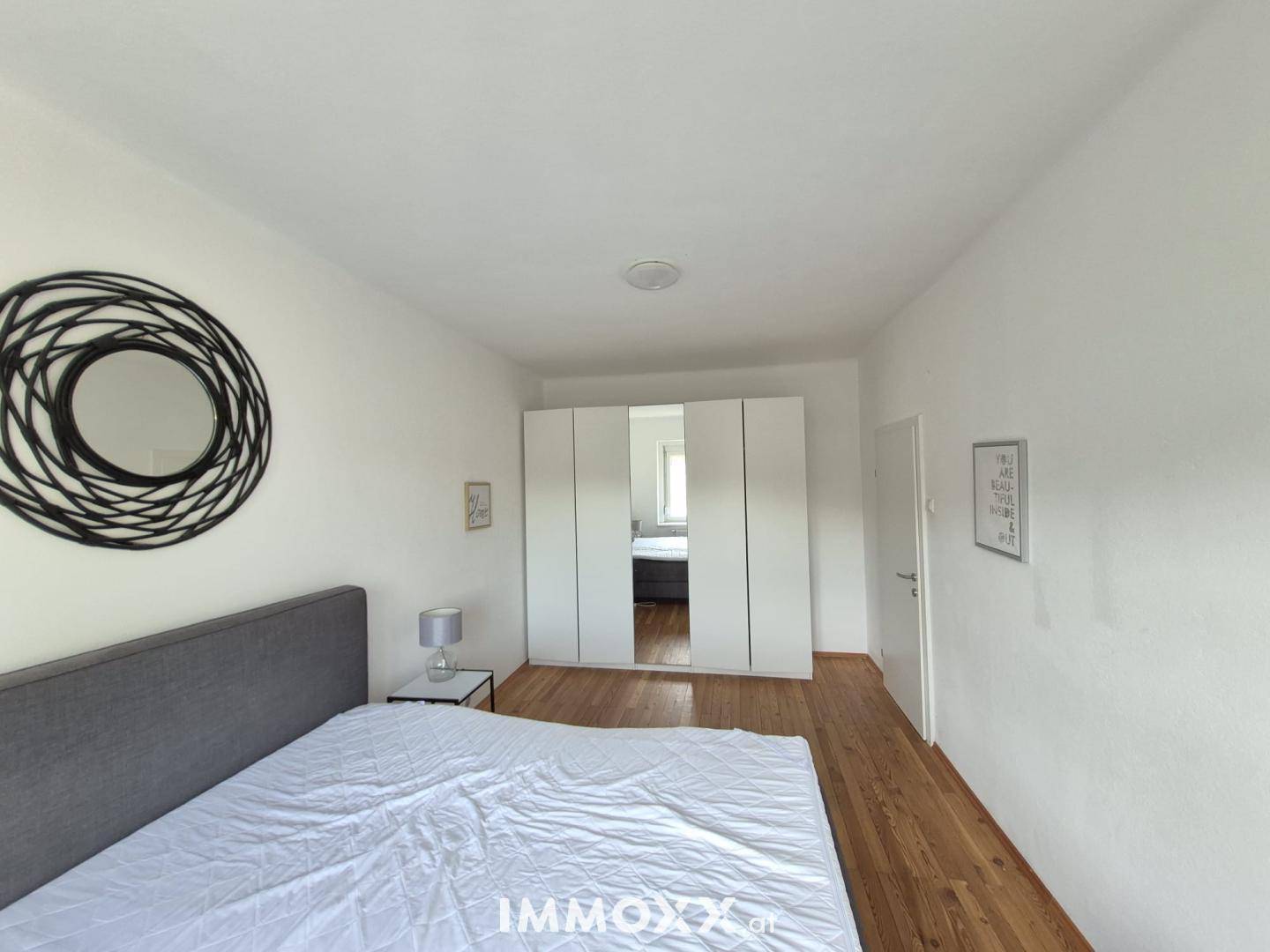 Helles Schlafzimmer mit Holzdielenboden und geräumigem Kleiderschrank mit Spiegeltüren.