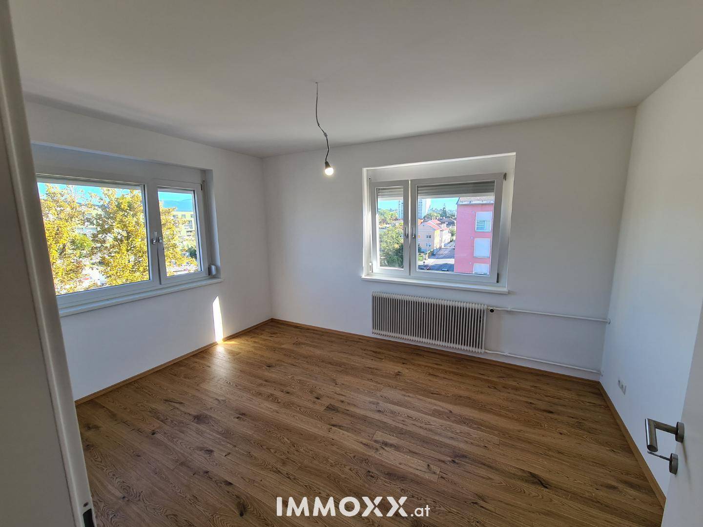 Lichtdurchflutetes Schlafzimmer mit Holzboden und zwei Fenstern, die eine angenehme Atmosphäre schaffen.