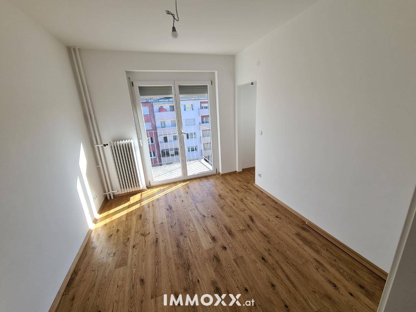 Sonniger Raum mit Holzboden und direktem Zugang zum Balkon, ideal für ein Schlafzimmer.