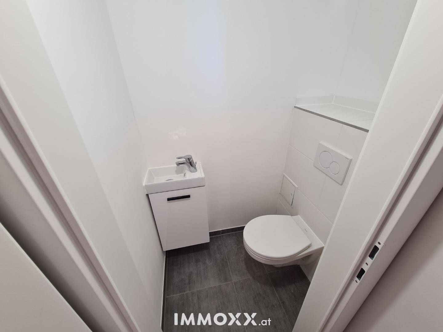 Modernes Gäste-WC mit wandhängender Toilette und kleinem Waschbecken, weiß gefliest.