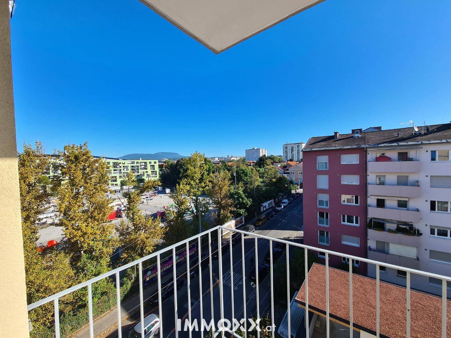 Weitblick vom Balkon über die Stadt und grüne Baumlandschaften an einem sonnigen Tag.