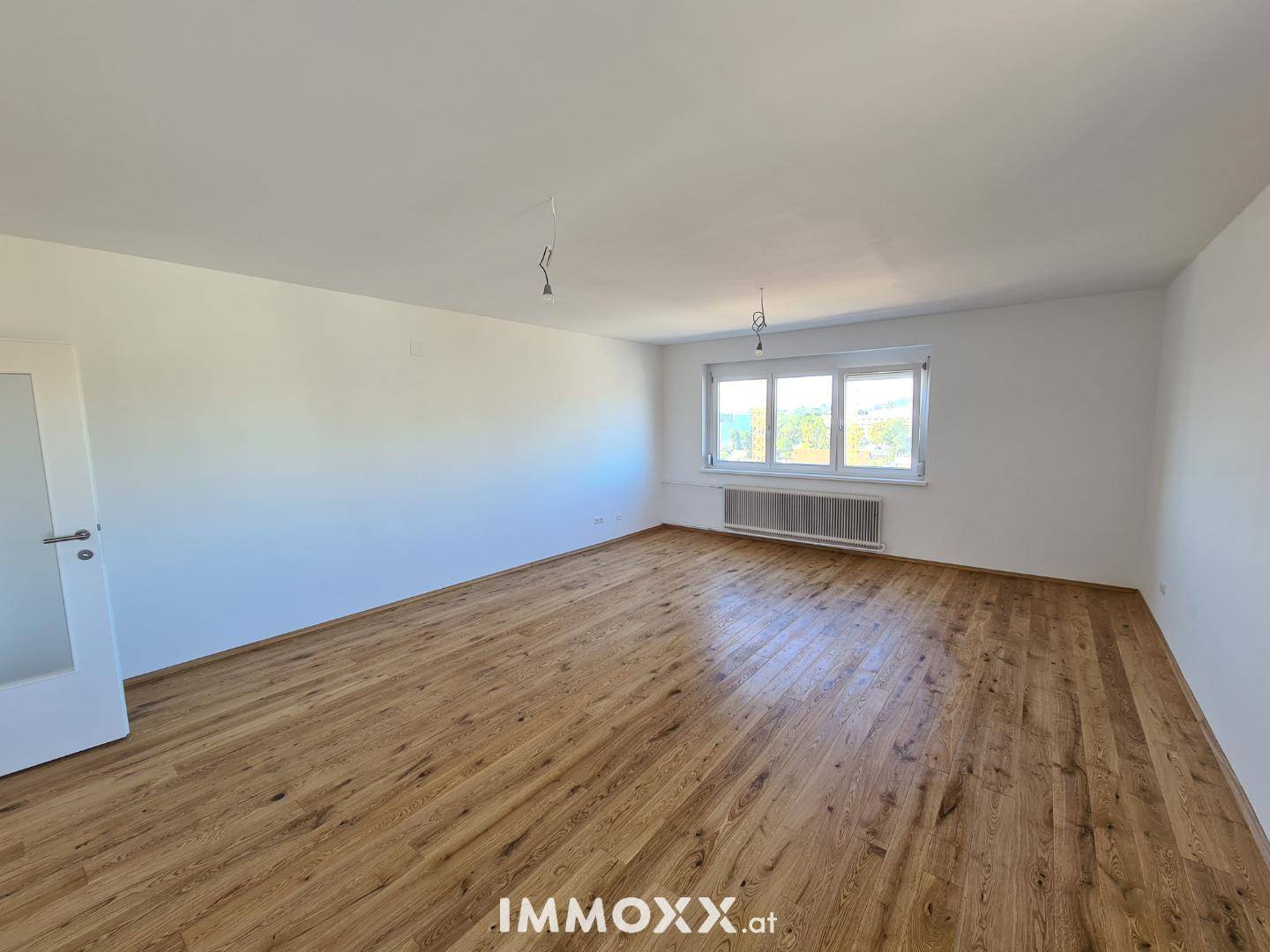 Helles, geräumiges Zimmer mit Holzboden und einem großen Fenster, das viel Licht spendet.