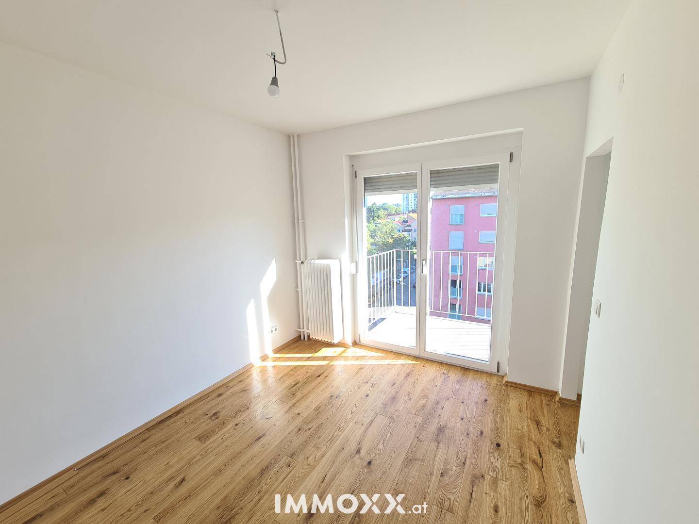 Helles Zimmer mit Holzboden und Zugang zu einem Balkon, ideal als Schlaf- oder Arbeitszimmer.