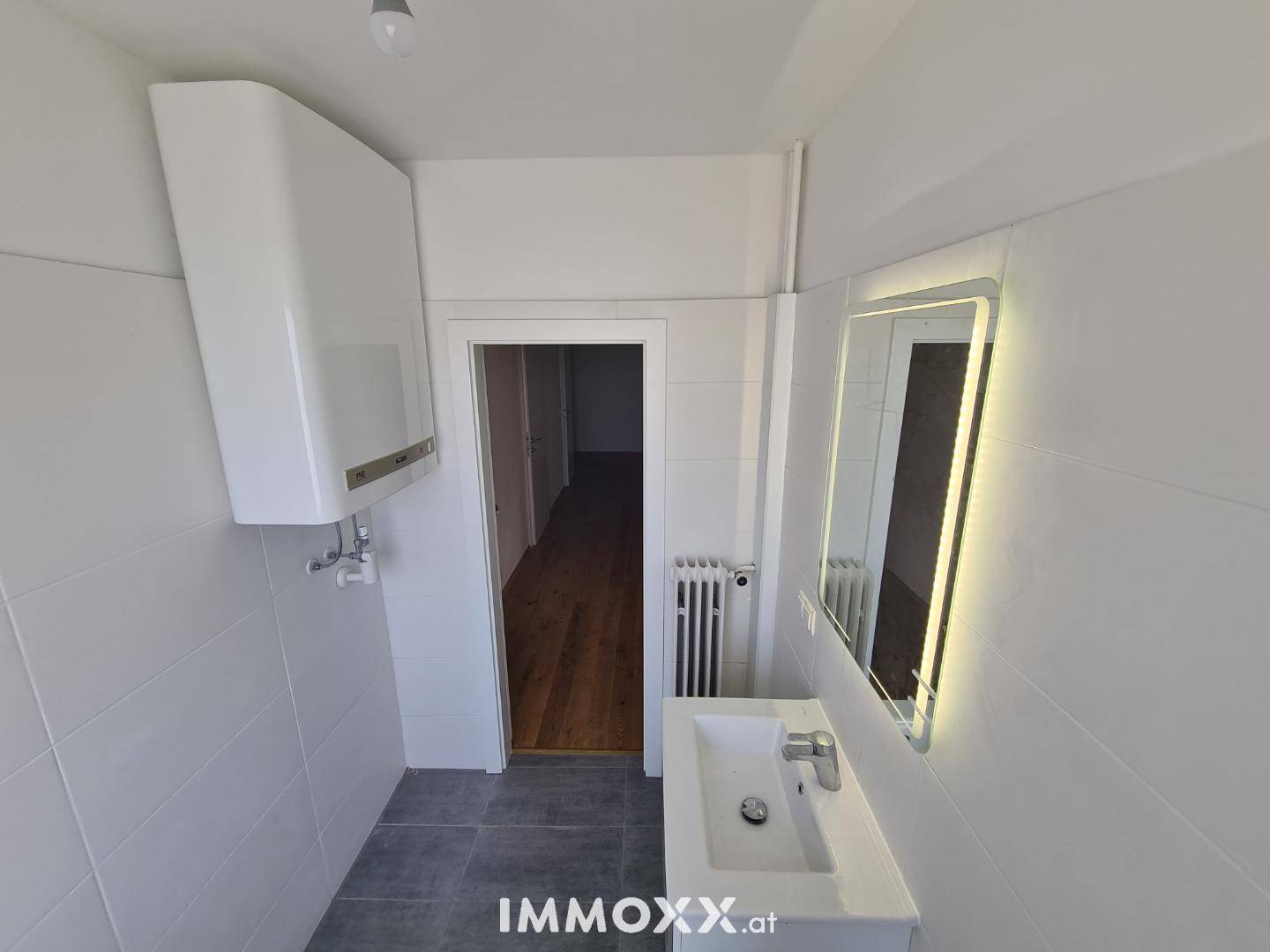 Modernes Badezimmer mit Waschbecken, beleuchtetem Spiegel und weiß gefliesten Wänden.