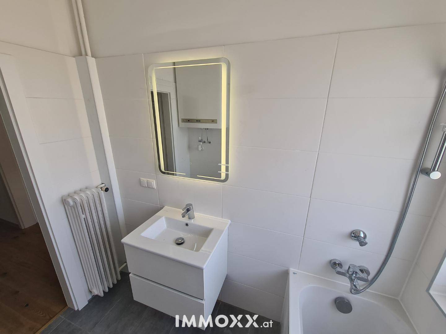 Modernes Badezimmer mit Waschbecken, beleuchtetem Spiegel und weißen Fliesen, inklusive Badewanne.