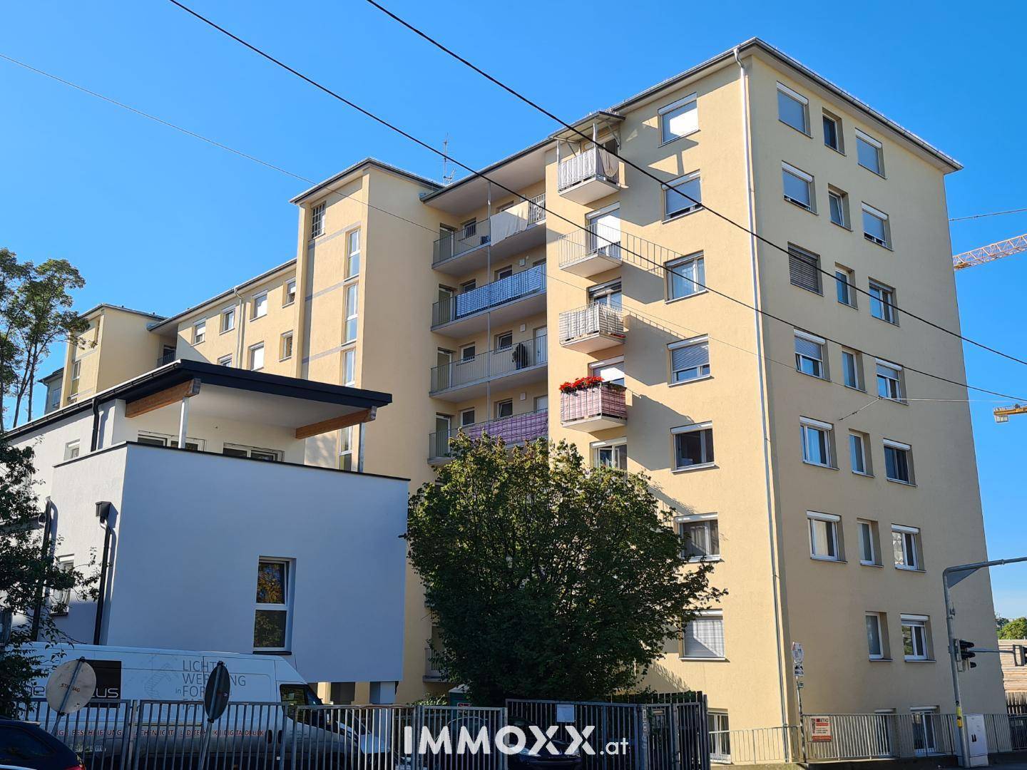 Mehrstöckiges Wohngebäude mit gelber Fassade und mehreren Balkonen unter blauem Himmel.