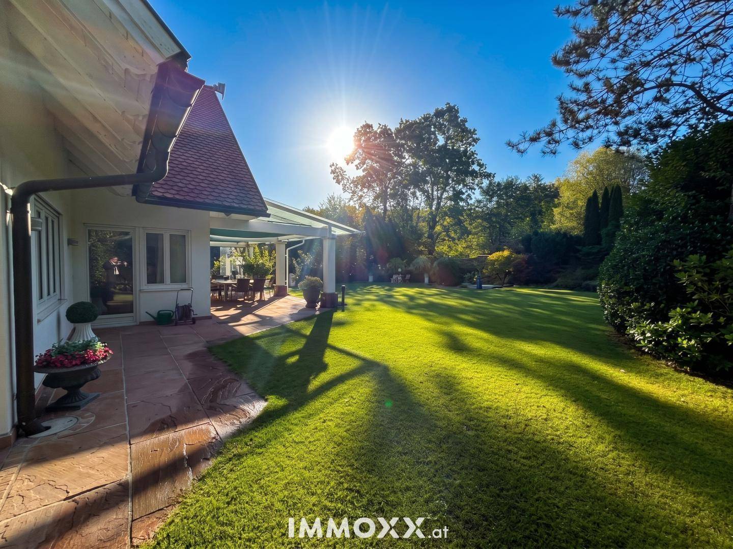 Weitläufiger, sonniger Garten mit gepflegtem Rasen und überdachter Terrasse am Haus.