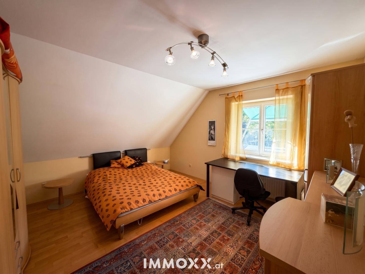 Schlafzimmer im Dachgeschoss mit Bett, Schreibtisch und Fenster, unter einer schrägen Decke.