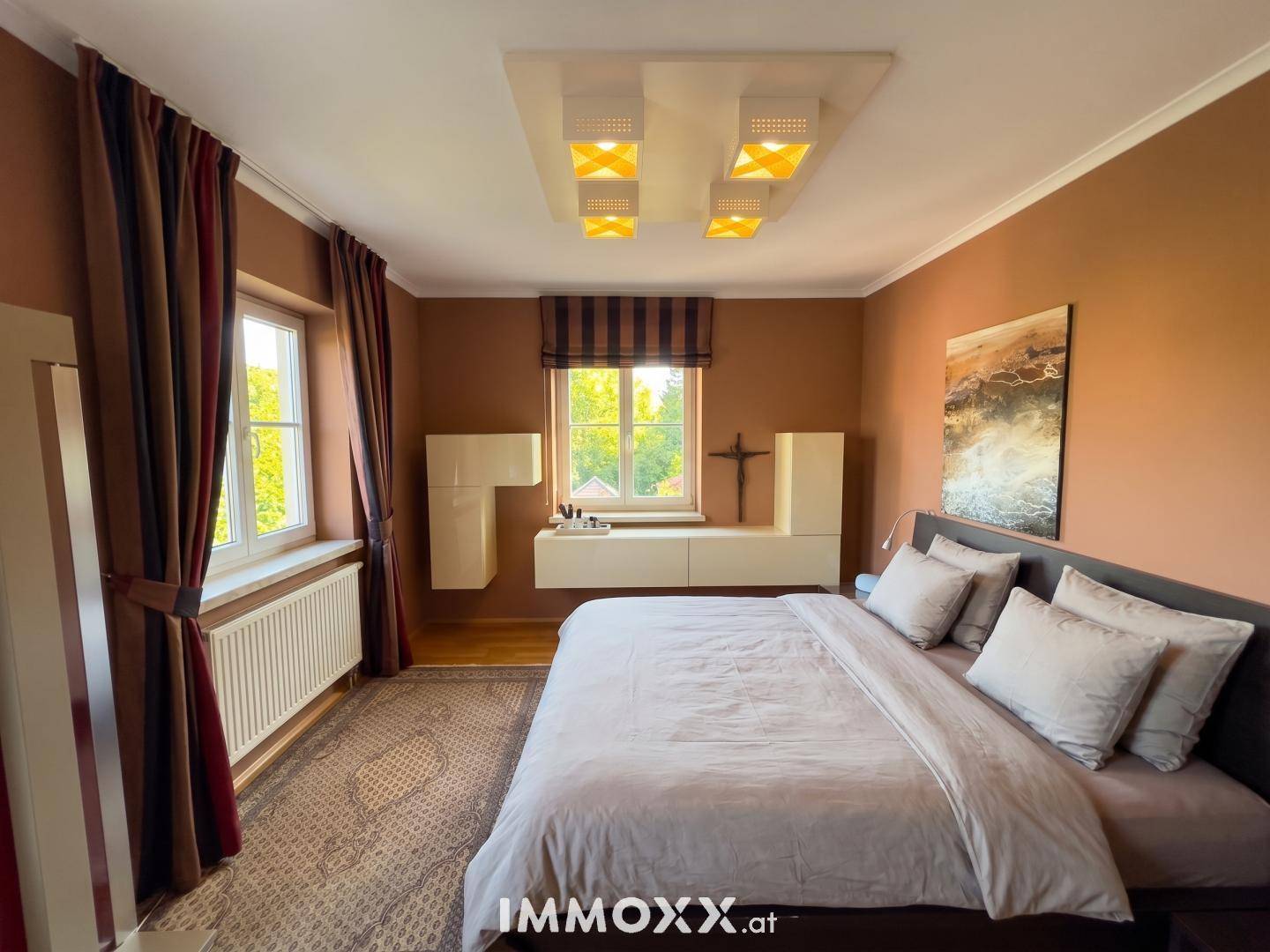 Gemütliches Schlafzimmer mit großem Bett, braunen Wänden und Fenstern für natürliche Belichtung.