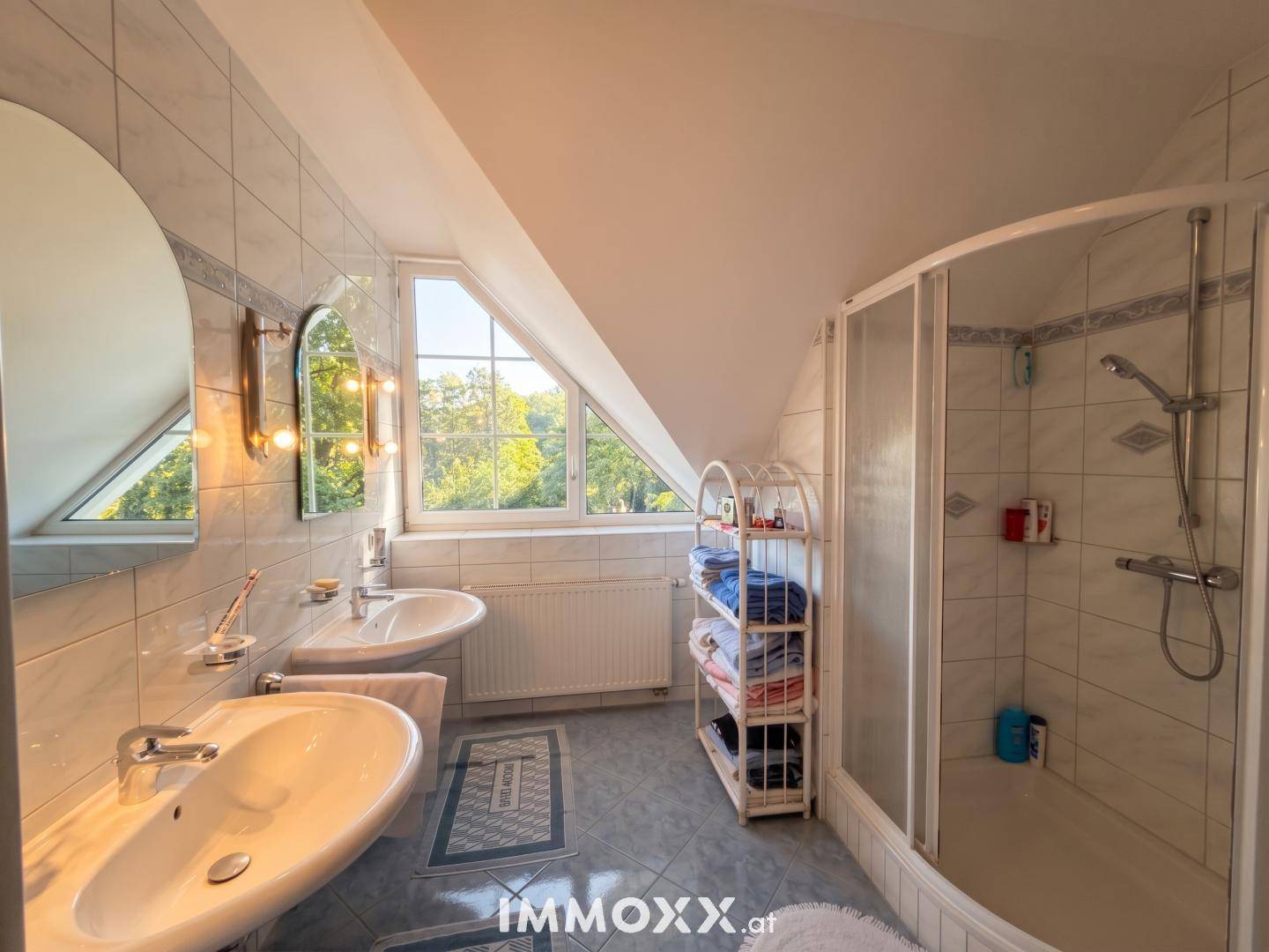 Badezimmer im Dachgeschoss mit Duschkabine, Doppelwaschbecken und dreieckigem Fenster.