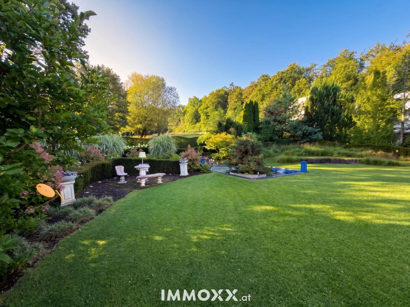 Weitläufiger, gepflegter Garten mit großer Rasenfläche, Zierbeeten und einem kleinen Pool im Hintergrund.