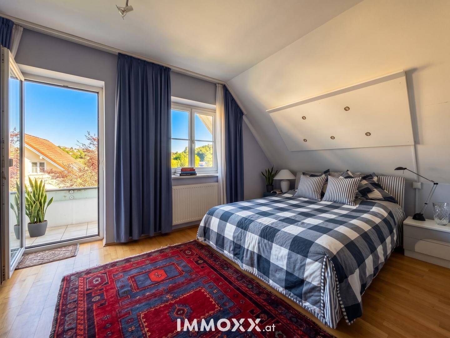 Schlafzimmer im Dachgeschoss mit Bett, Holzfußboden und Zugang zu einem kleinen Balkon.