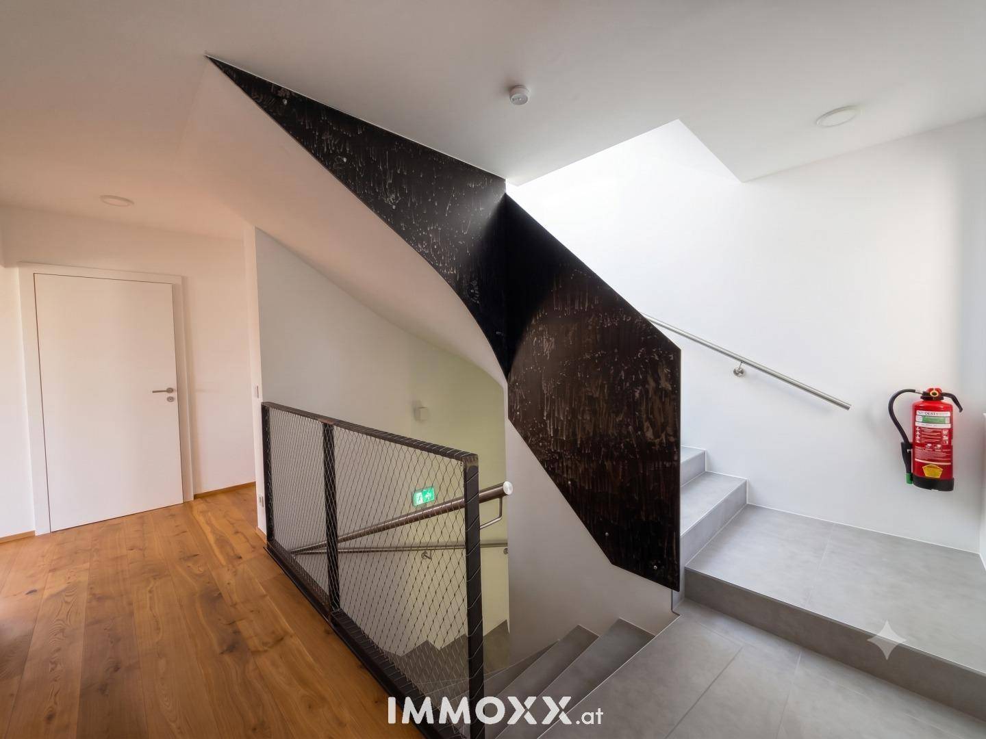 Modernes Treppenhaus mit Holzboden, Metallgeländer und klaren Linien im Eingangsbereich.