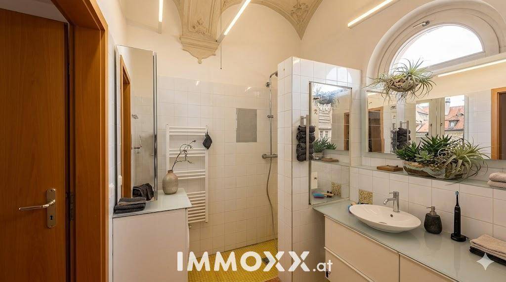 Badezimmer mit gewölbter Decke, Dusche, Einzelwaschbecken und einem großen Rundbogenfenster.